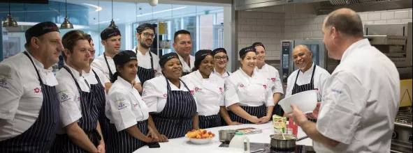 A group of chefs learning from an experienced chef at Elior's chef school