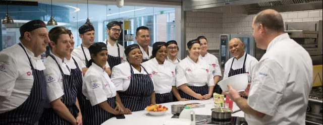 A group of chefs learning from an experienced chef at Elior's chef school